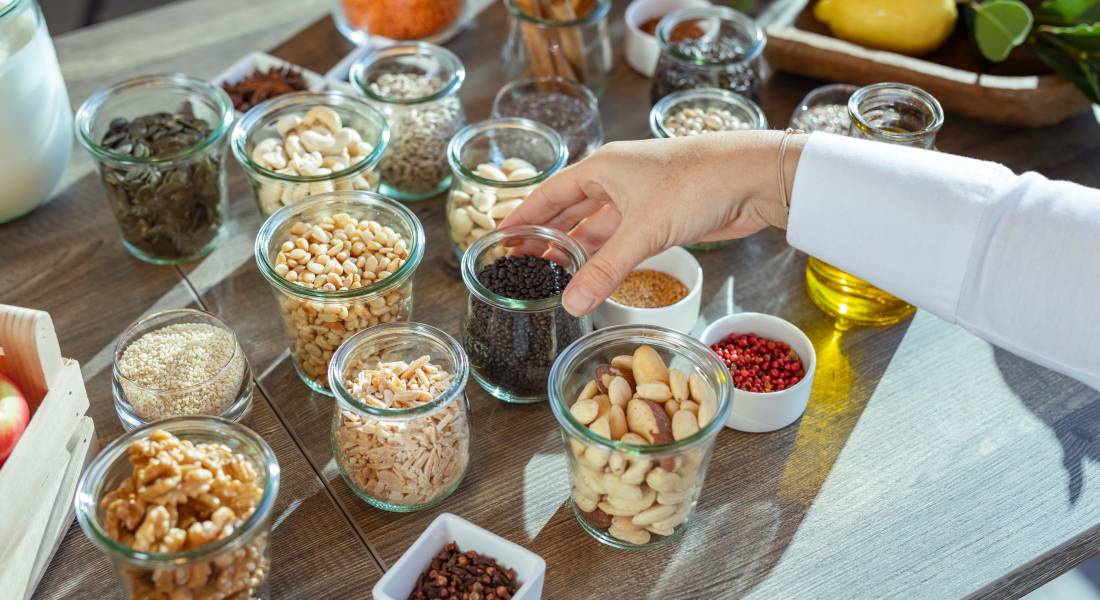 Verschiedene natürliche Lebensmittel sind in Gläsern auf einem Holztisch platziert.